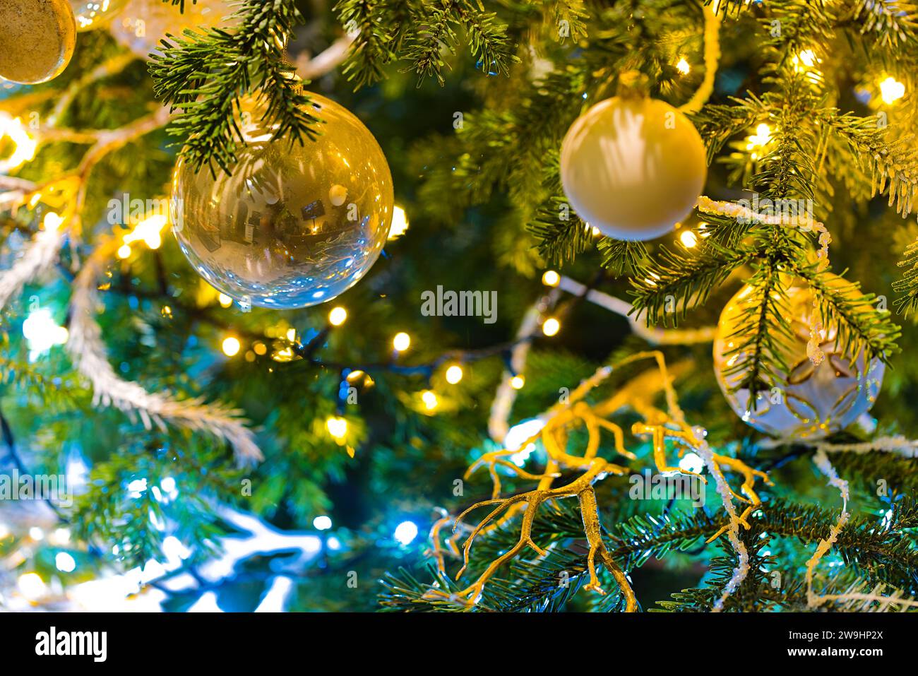 Des ornements suspendus illuminent un sapin de Noël, entouré par la lueur douce des lumières de Noël floues. Banque D'Images