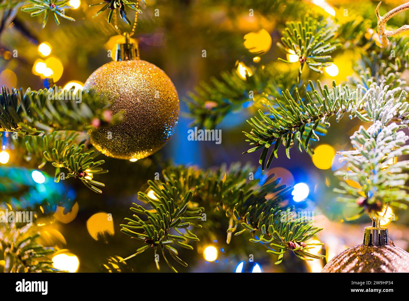Des ornements suspendus illuminent un sapin de Noël, entouré par la lueur douce des lumières de Noël floues. Banque D'Images