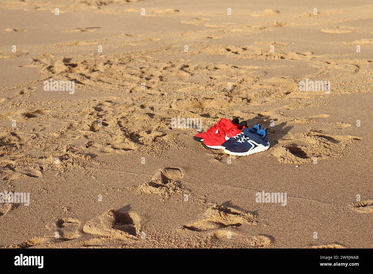 Deux paires de baskets, une bleue et l'autre rouge, sur le sable de la plage. Banque D'Images