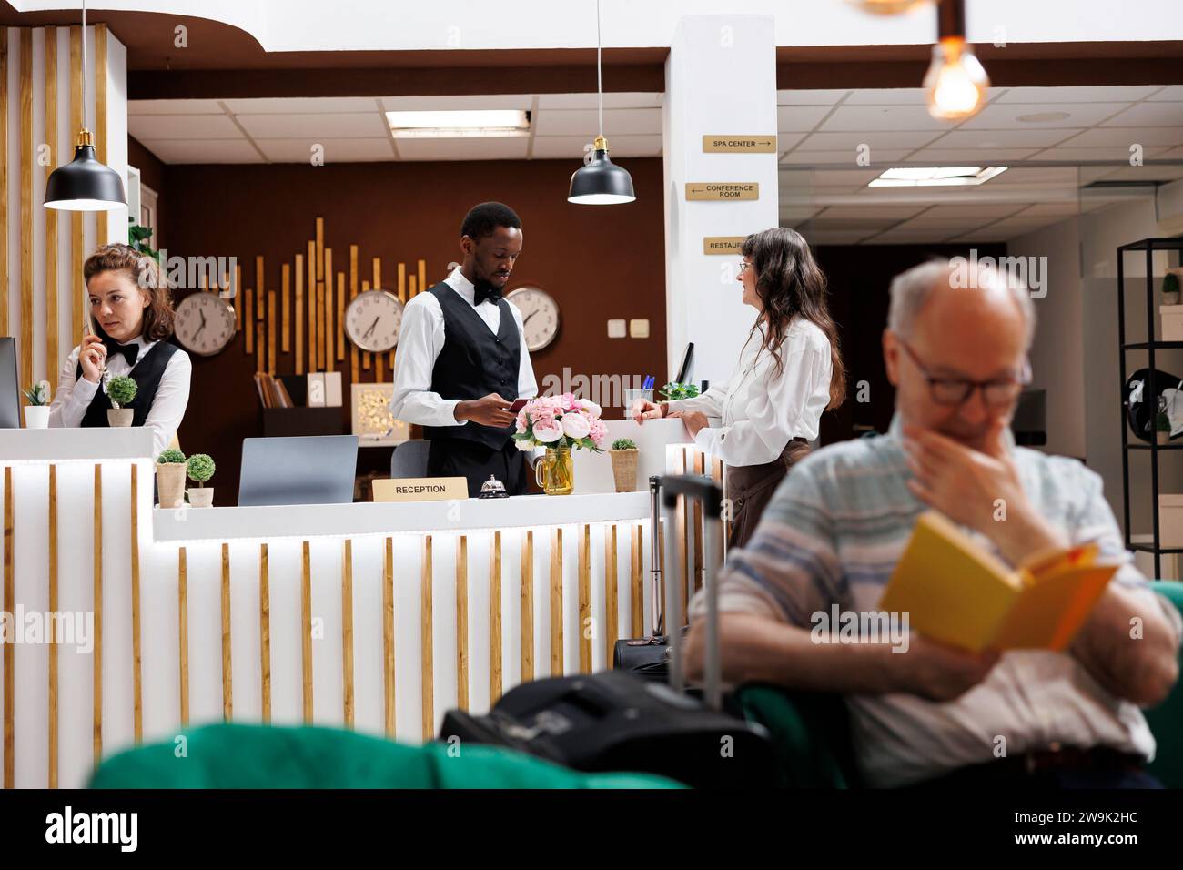 Concierge masculin vérifie le passeport de la femme senior à l'arrivée à la réception de l'hôtel. L'employé aide à l'enregistrement et à la vérification des pièces d'identité. Expérience agréable et accueillante pour les clients âgés dans le salon. Banque D'Images