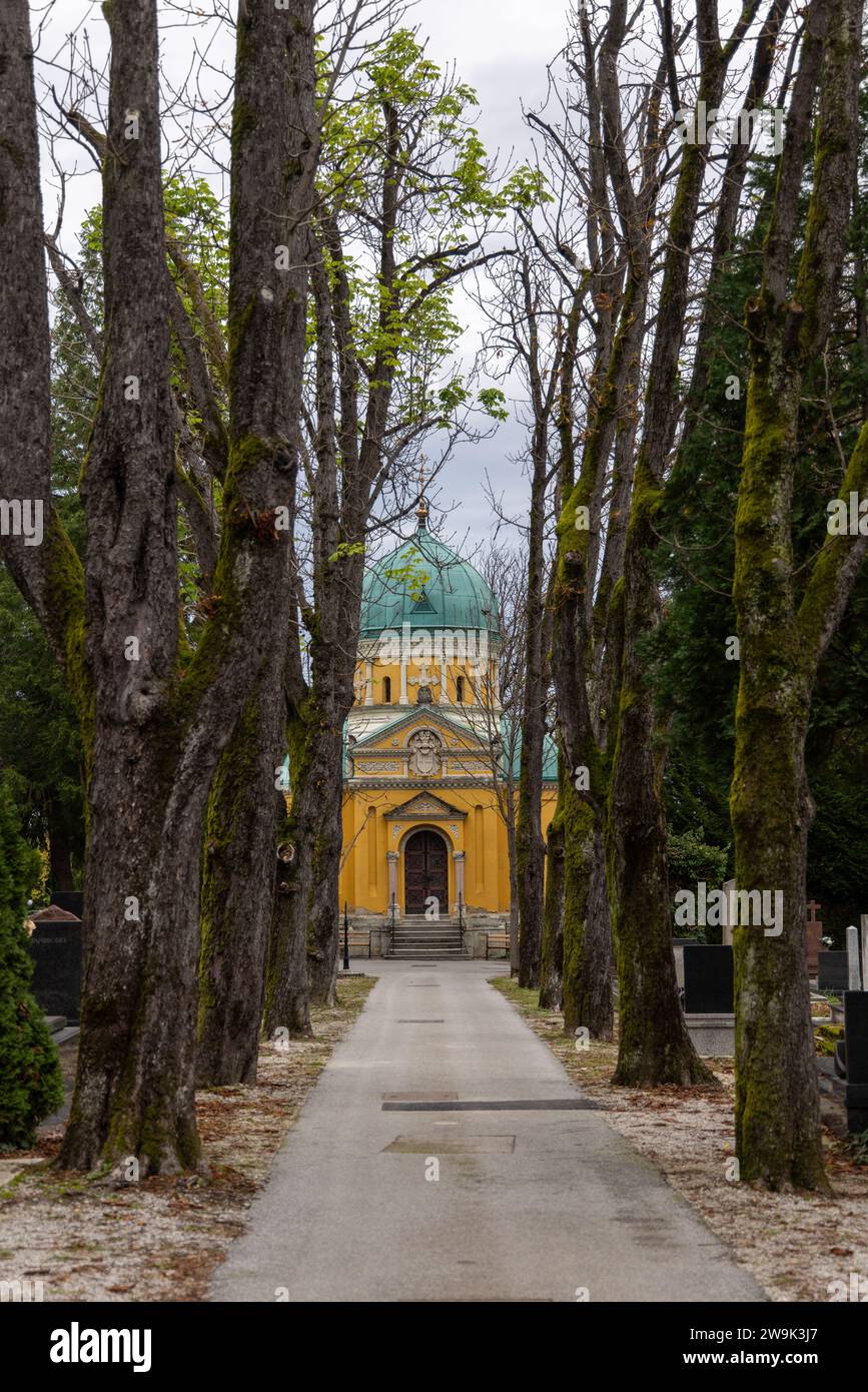 Ruelle bordée d'arbres vers le bâtiment jaune de la chapelle orthodoxe des saints apôtres Saints Pierre et Paul sur le cimetière Mirogoj à Zagreb, Croatie Banque D'Images