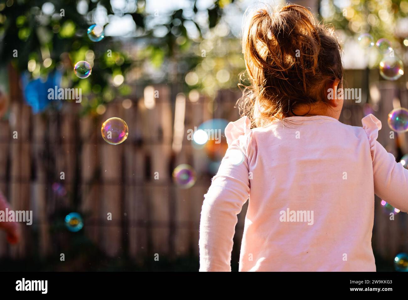 Petit enfant d'âge préscolaire chassant des bulles dans la lumière dorée du matin Banque D'Images