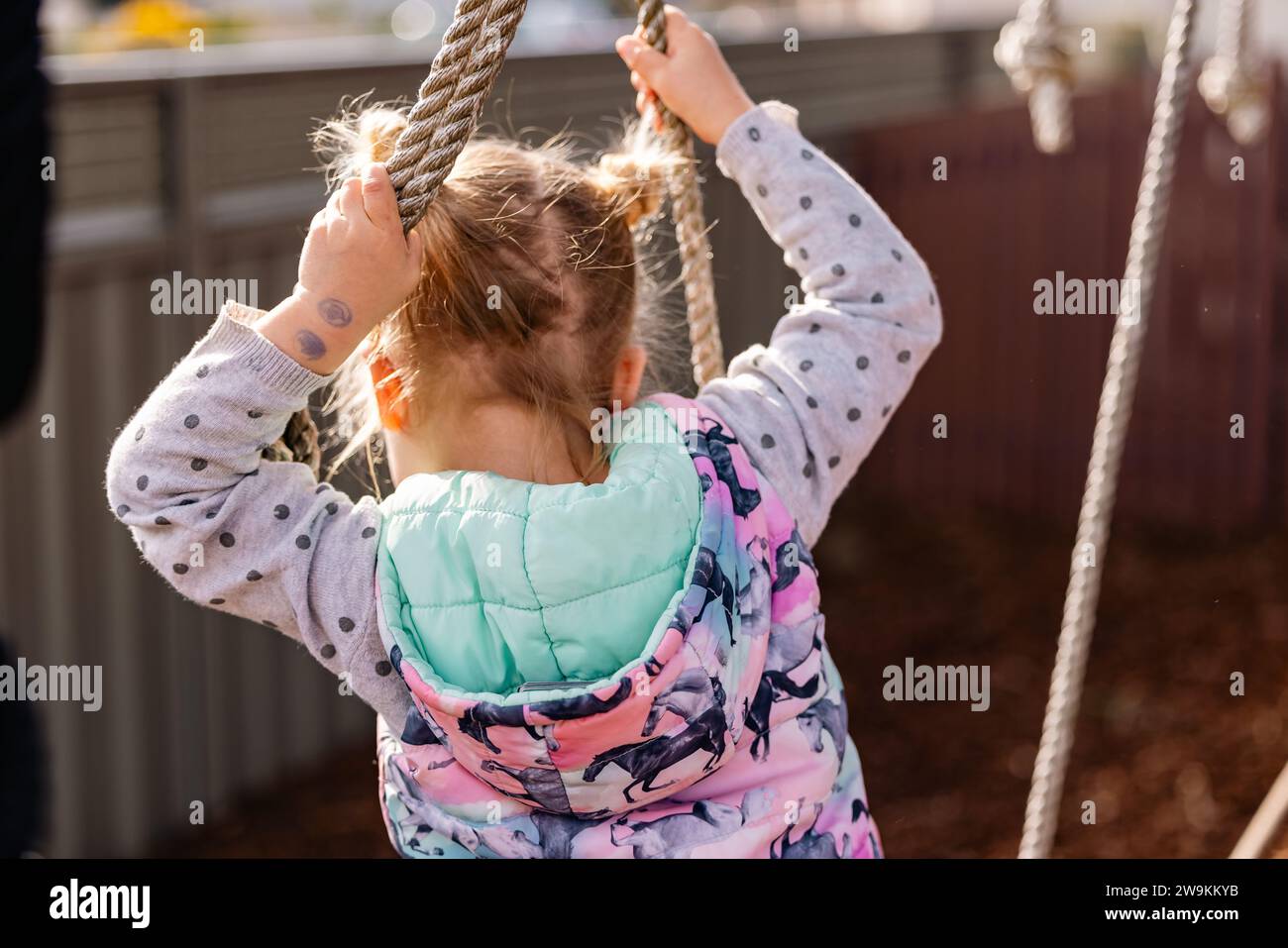 Petite fille jouant sur le matériel d'escalade de maternelle, pas de visage visible Banque D'Images