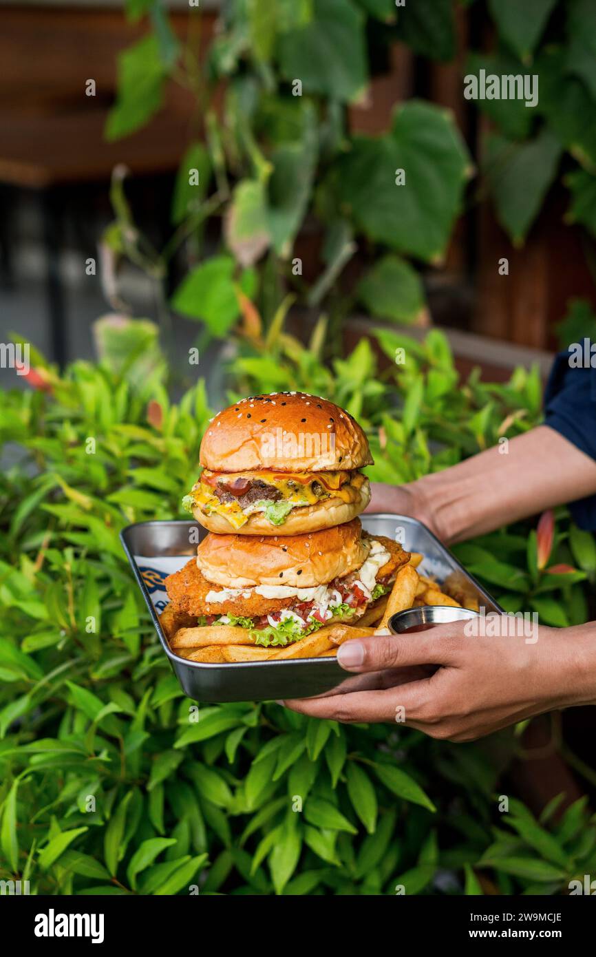 Sur cette photo, la main d'une personne tient un hamburger avec diverses saveurs délicieuses. Banque D'Images