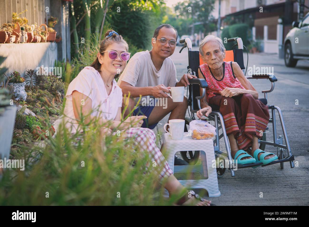 famille asiatique avec une grande maman assise sur une chaise roulante profiter du café du matin au village de la maison Banque D'Images