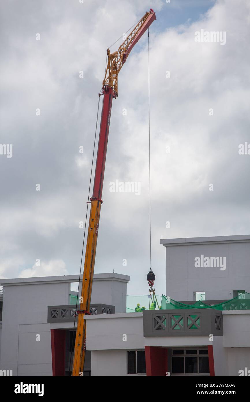 Travaux industriels déployer une grue soulevant des marchandises lourdes ou déchargeant de l'équipement sur le toit d'un immeuble résidentiel, Singapour. Banque D'Images