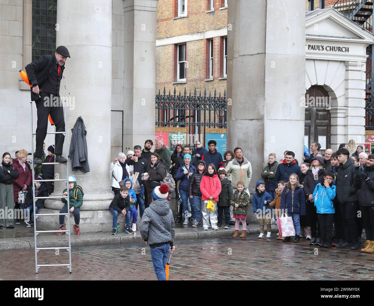 Par temps de pluie, un artiste de rue sur une échelle divertit les spectateurs à Covent Garden, Londres, Royaume-Uni Banque D'Images