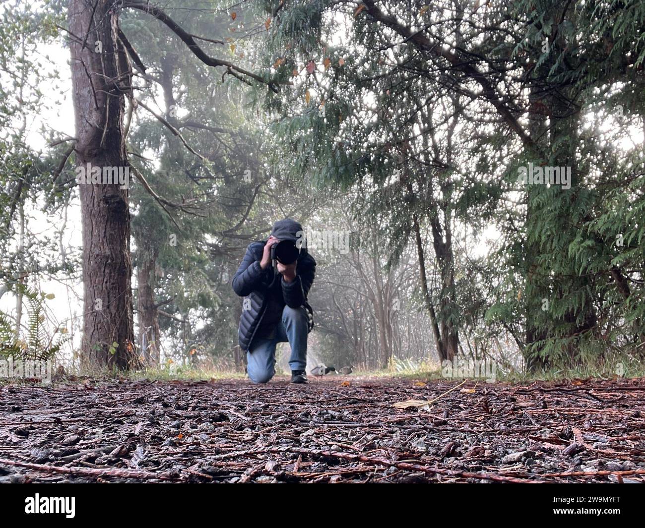 Homme accroupi dans un paysage rural prenant une photo avec un appareil photo à objectif long, Vancouver, Colombie-Britannique, Canada Banque D'Images