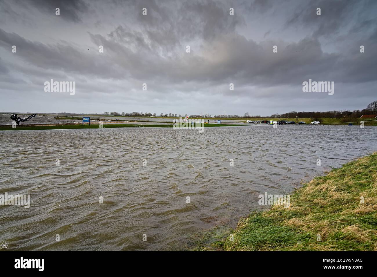 lac inonder la plage avec kite surfeurs, parking avec des voitures et les prairies à l'extérieur de la digue en raison des hautes eaux et fortes rafales de vent avec pluie Banque D'Images