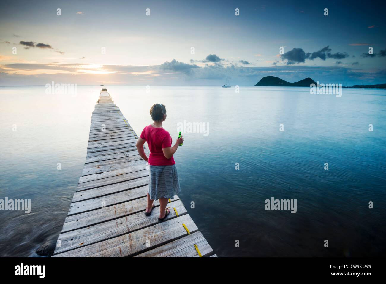 Une femme profite du coucher de soleil sur la mer des Caraïbes sur un quai de l'hôtel Portsmouth Beach dans la ville de Portsmouth sur l'île de la Dominique. Banque D'Images