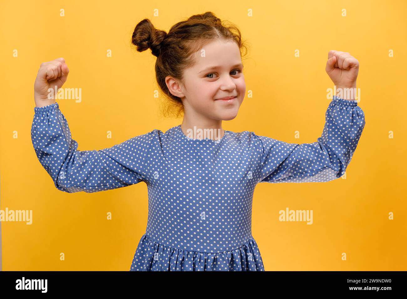 Portrait de petite fille confiante souriant joyeusement et levant les poings serrés, tendant les muscles, se sentant forte et pleine d'énergie après avoir mangé Healt Banque D'Images