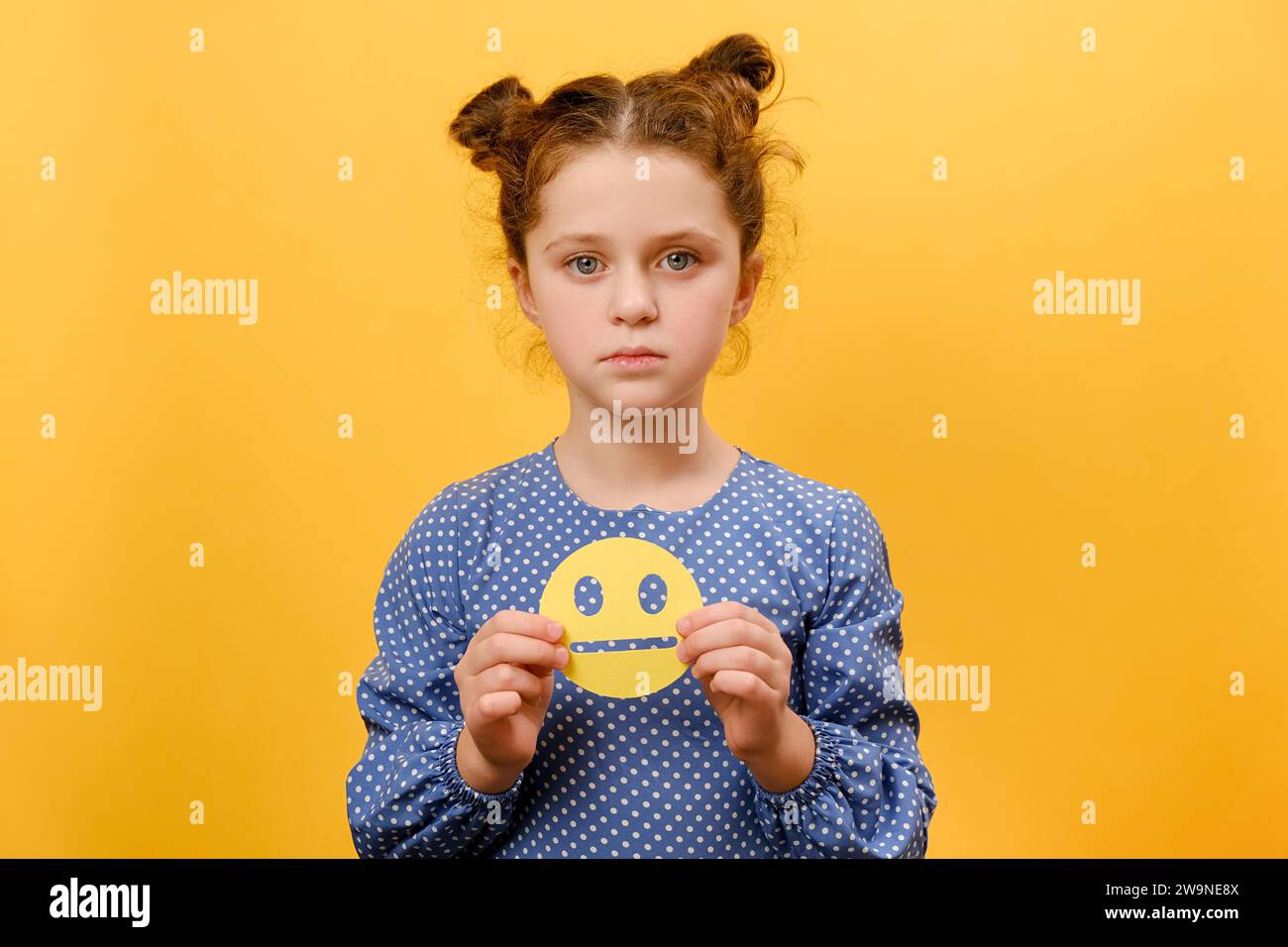 Portrait d'une fille caucasienne préadolescente malheureuse tenant une émoticône jaune triste, regardant la caméra, posant isolé sur un backgro de couleur jaune Uni Banque D'Images
