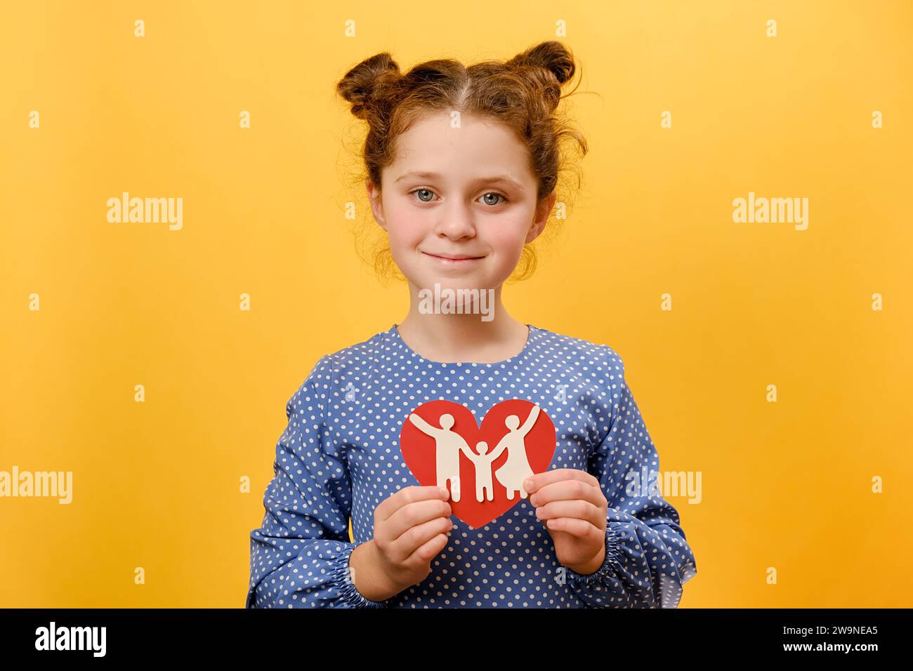 Portrait d'heureux enfant de préadolescence tenant la silhouette de papier blanc de la famille sur le coeur, souriant et regardant la caméra, posant isolé sur jaune Uni c Banque D'Images