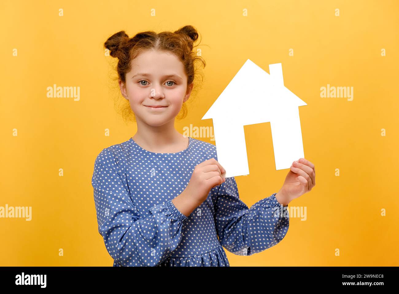 Portrait d'heureux mignon petit enfant de 8 ans tenant le modèle de maison blanche sur les mains, regardant la caméra, posant isolé sur le mur de fond de couleur jaune Banque D'Images