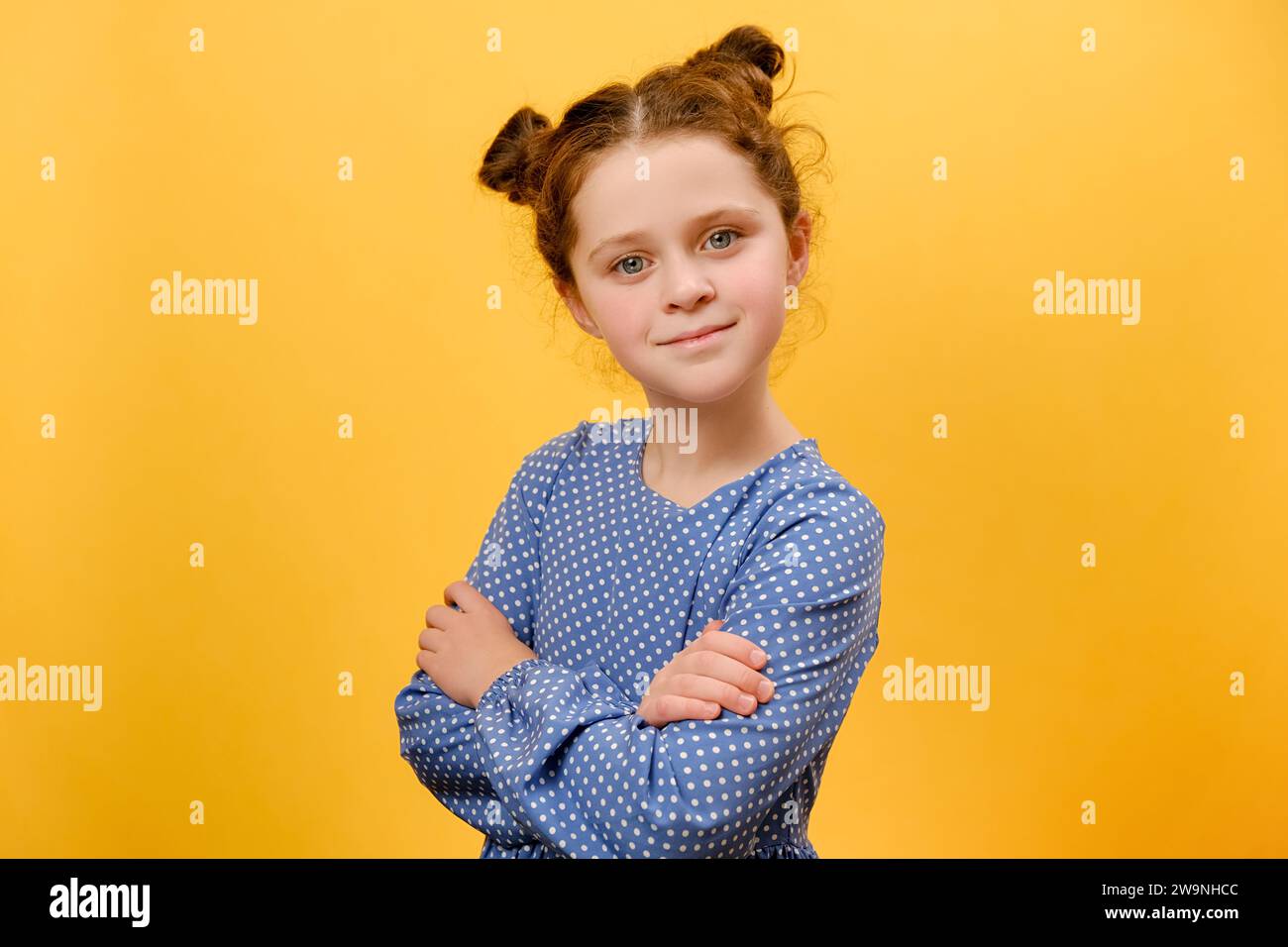 Portrait de mignon souriant enfant de fille de préadolescence avec les mains croisées heureux regardant la caméra, posant isolé sur le mur de fond de couleur jaune dans le studio avec Banque D'Images