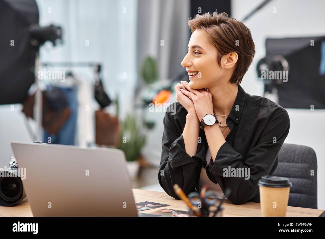 jeune femme joyeuse en tenue décontractée assise au bureau dans son studio photo et regardant loin Banque D'Images