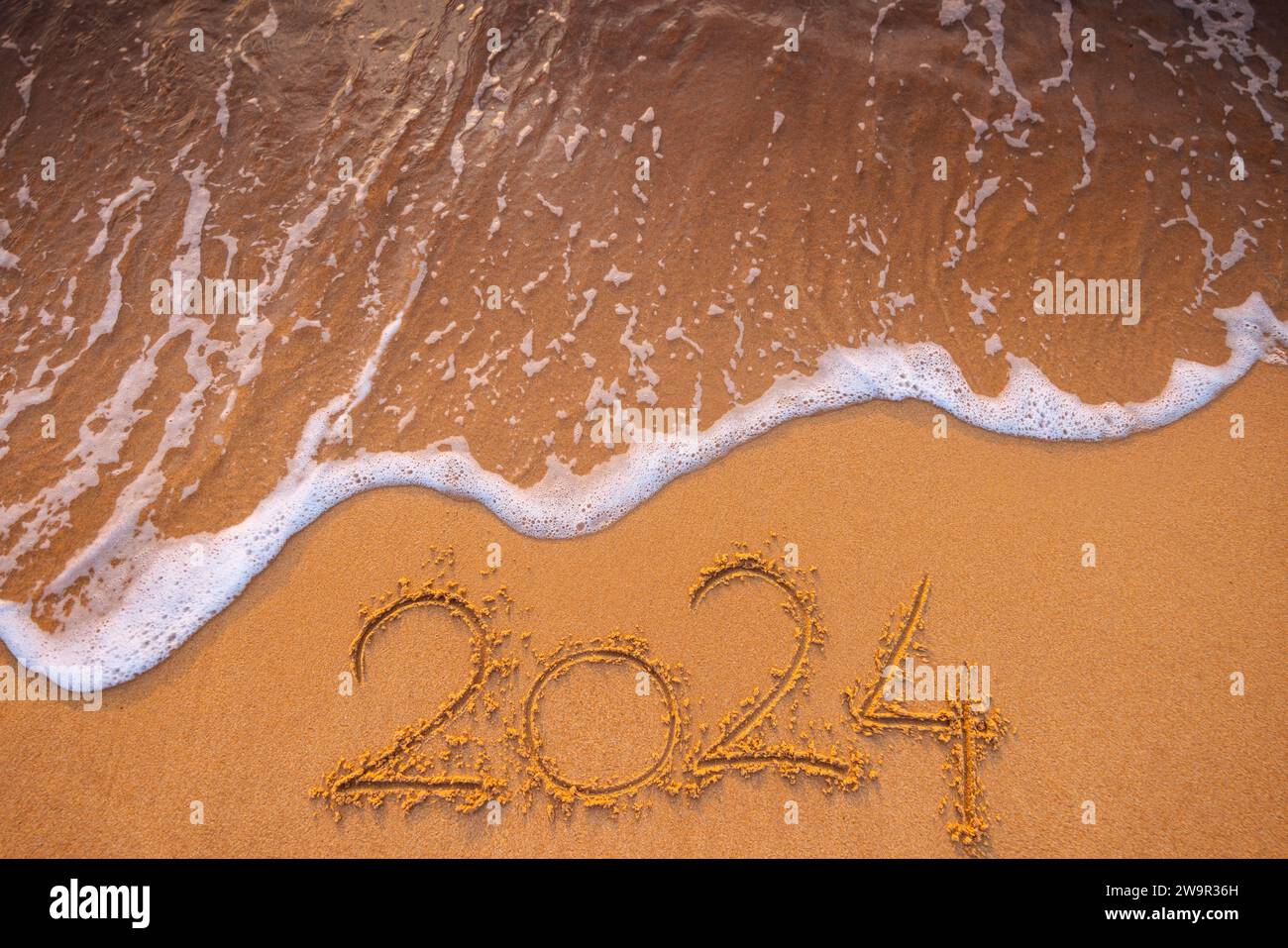 Bonne année 2024 concept, lettrage sur la plage. Texte écrit sur la plage de la mer au lever du soleil. Banque D'Images