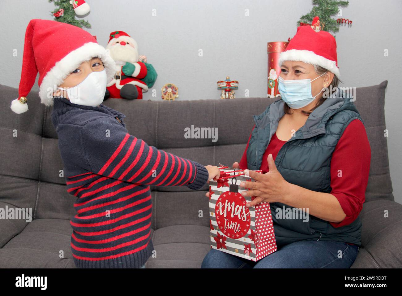 Grand-mère et enfant avec masque de protection et chapeau du père noël, cadeaux et décorations de Noël, nouveau covid-19 normal Banque D'Images