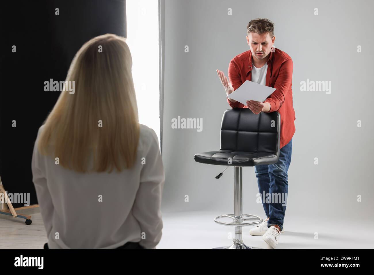 Homme avec script se produisant devant le directeur de casting sur fond gris clair en studio Banque D'Images