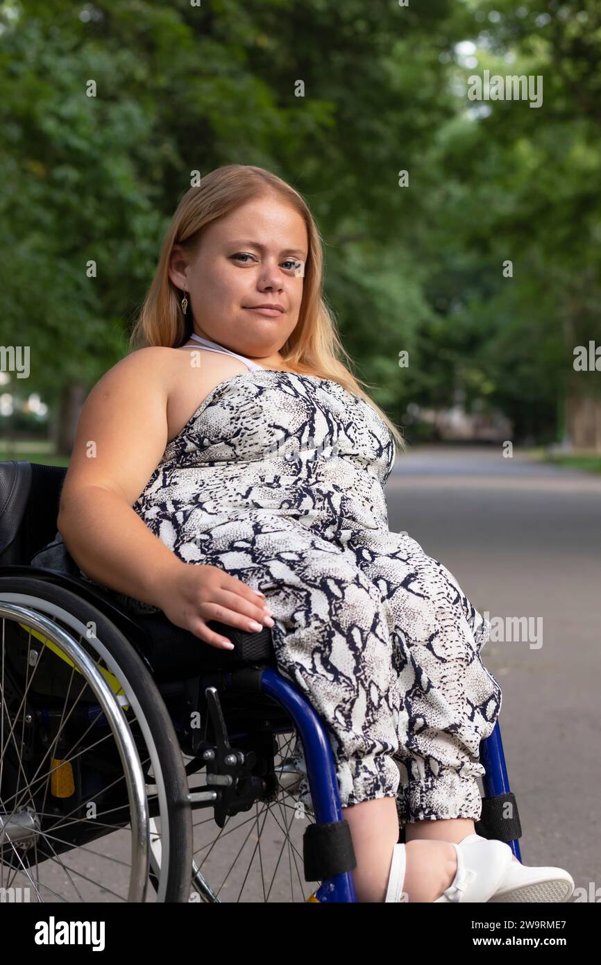 Journée internationale des fauteuils roulants , le 1 mars souriant. Jolie jeune femme avec stature courte assise dans fauteuil roulant en plein air. Garez-vous sur fond. Personne Banque D'Images