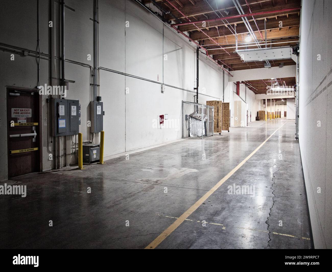 Couloir du grand entrepôt industriel avec boîtes électriques et porte d'évacuation incendie visible. Banque D'Images