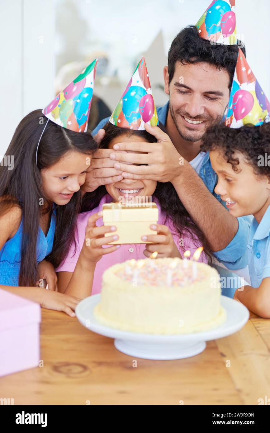 Gâteau d'anniversaire, enfant et cadeau avec les yeux couverts, surprise et famille heureuse pour la célébration, frères et sœurs et papa. Chanter, sourire et aimer avec des cadeaux Banque D'Images