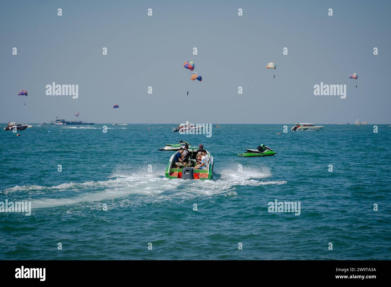 Pattaya, Thaïlande. 27 décembre 2023. Un bateau transportant des touristes pour des activités nautiques est vu sur la mer, avec en arrière-plan des touristes jouant au parachute ascensionnel à Pattaya Beach. Pattaya Beach est une destination touristique bien connue en Thaïlande. Mais alors que la ville de Pattaya a acquis une réputation pour sa vie nocturne animée et ses options de divertissement, elle ne se concentre pas uniquement sur la restauration pour les voyageurs solo masculins. Au-delà de sa vie nocturne, la ville attire divers touristes, y compris les familles, les couples et les individus de tous âges, pour le shopping, les activités nautiques et la détente en bord de mer. (Image de crédit : © Nathalie Jamo Banque D'Images