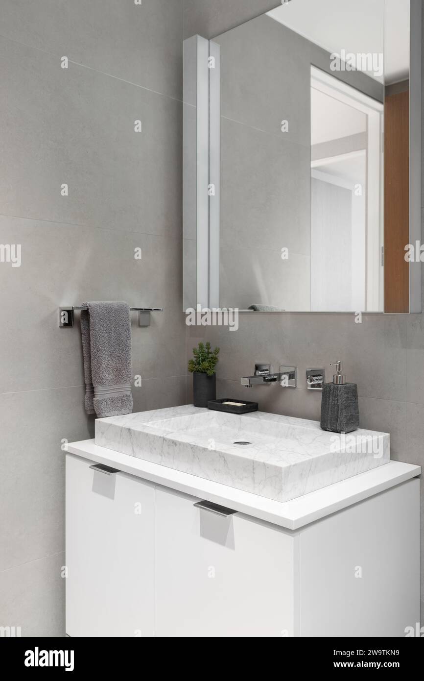 Un lavabo de salle de bains avec un lavabo en marbre blanc, une armoire blanche et des murs en carreaux de pierre grise. Banque D'Images