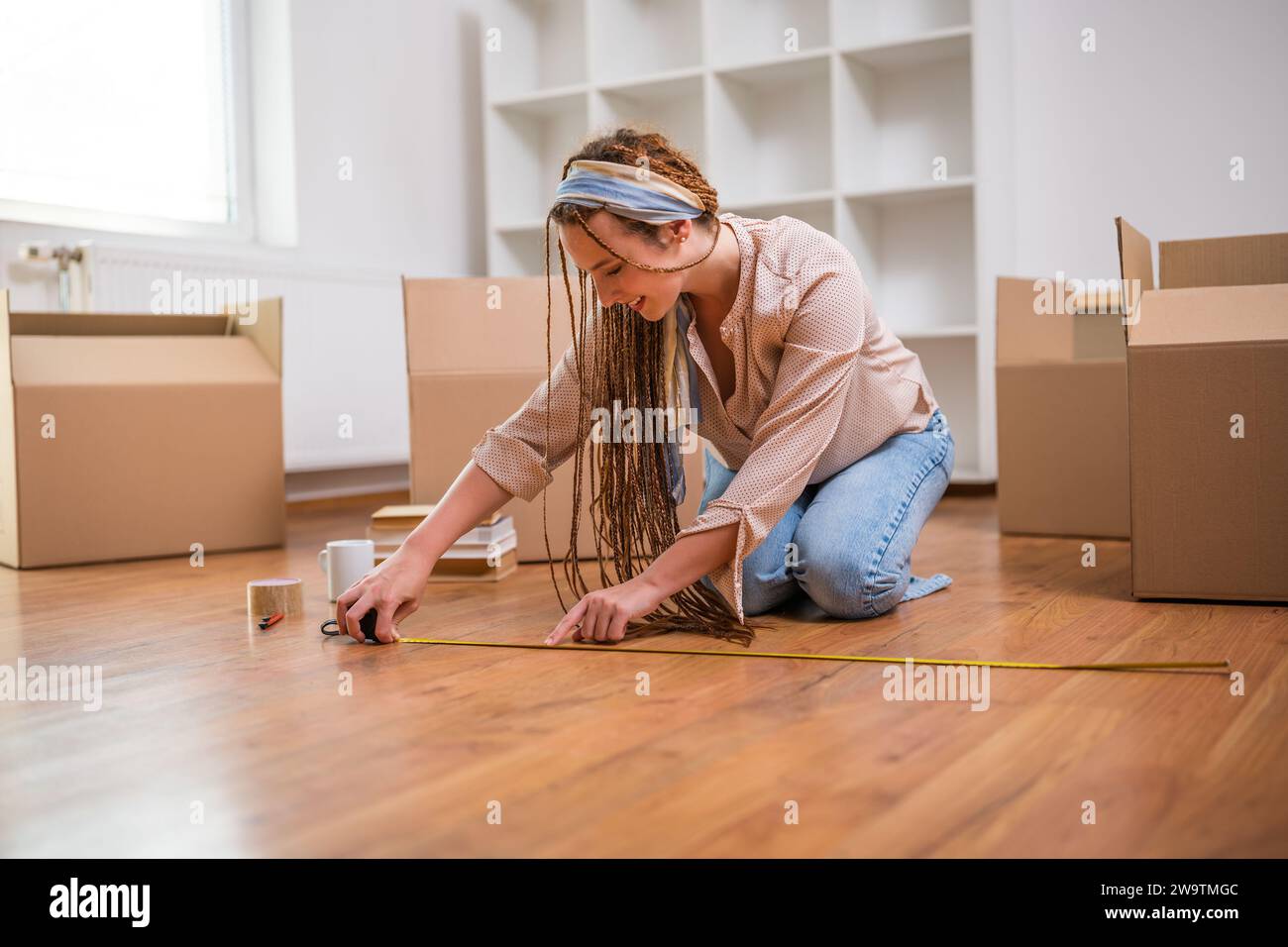 Femme au gingembre moderne avec tresses déménageant dans la nouvelle maison et mesurant le sol. Banque D'Images