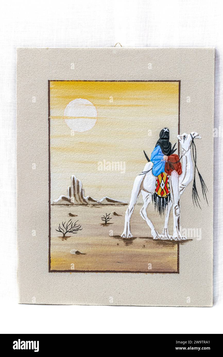 Peinture au sable d'un cavalier sahraoui portant un foulard noir traditionnel avec lettre x sur un chameau blanc avec des vêtements, cercle de soleil dans un ciel jaune. Banque D'Images