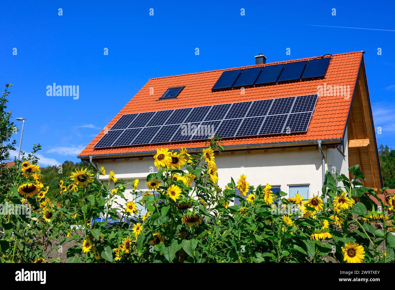 Toit solaire moderne sur une maison individuelle nouvellement construite contre un ciel bleu avec des tournesols au premier plan Banque D'Images