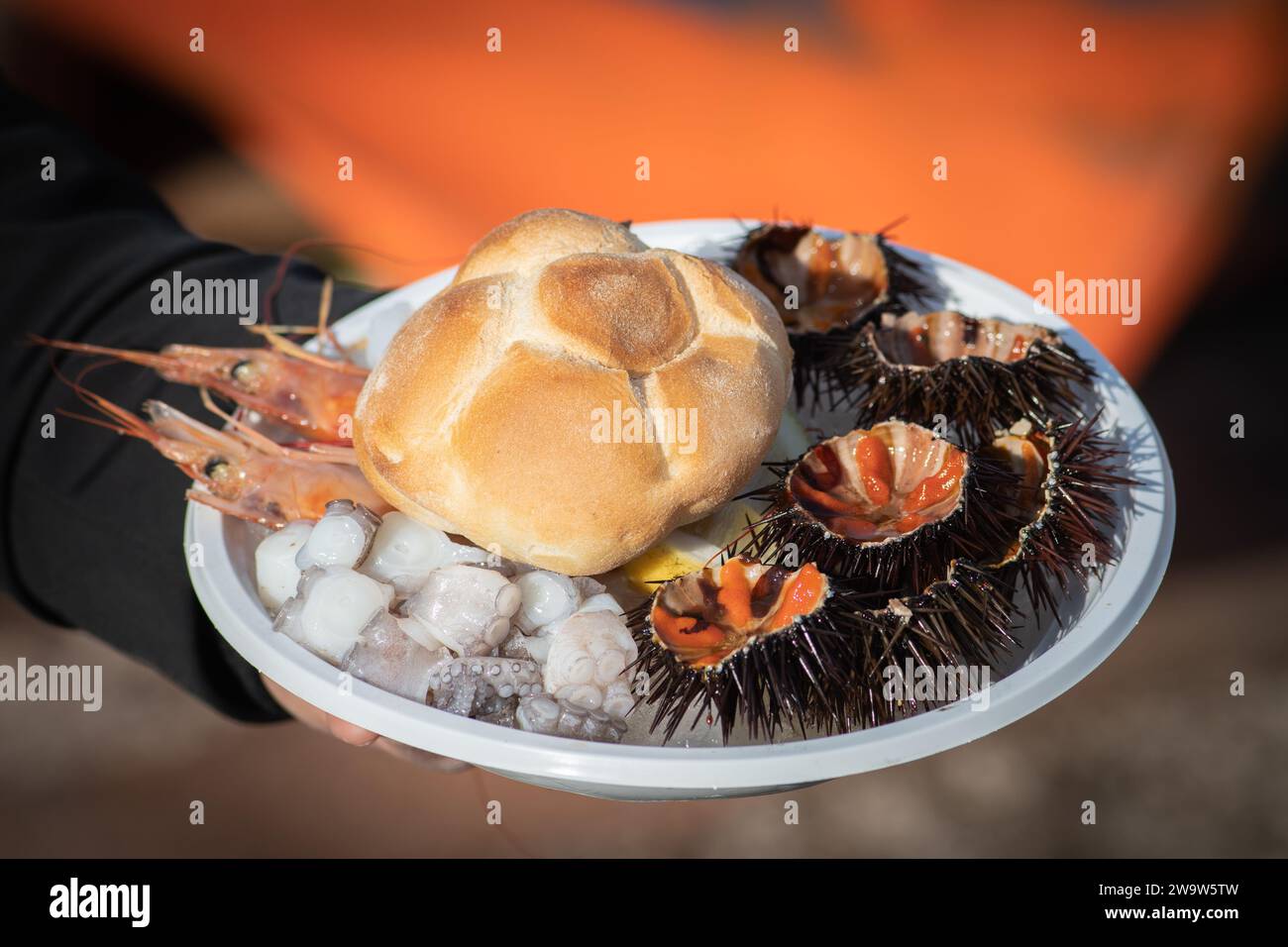 Assiette avec oursins de mer ouverts, morceaux crus de poulpe, seiches et crevettes ou scampi prêts à manger avec du pain dans un marché de nourriture de rue à Bari, Pouilles Banque D'Images