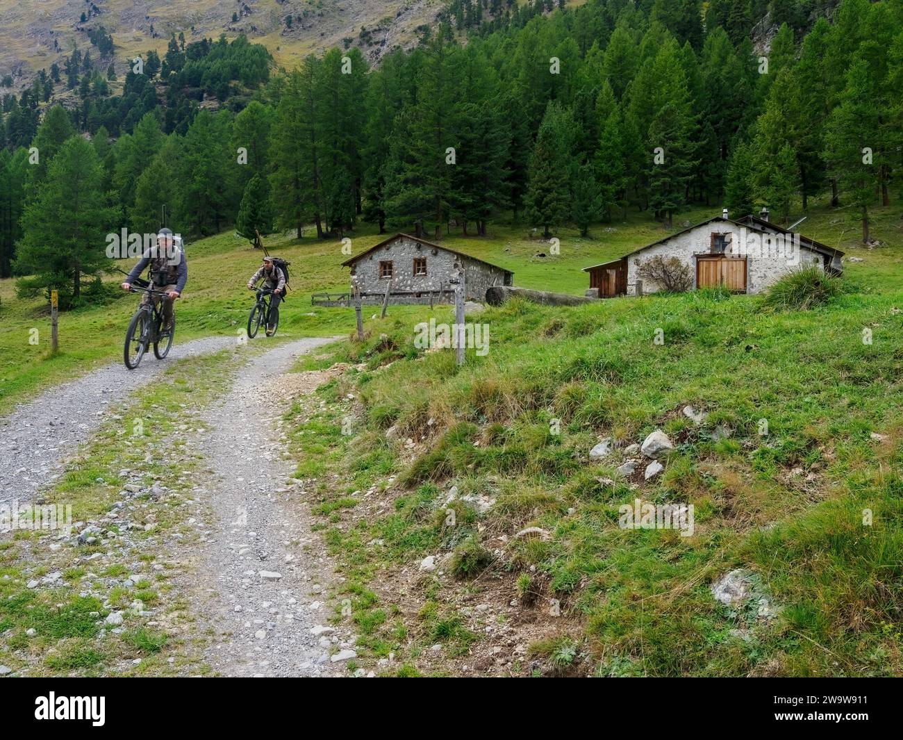 Les motards passent devant des granges en pierre dans la vallée de Roseg, Alpine St. Moritz, Suisse Banque D'Images