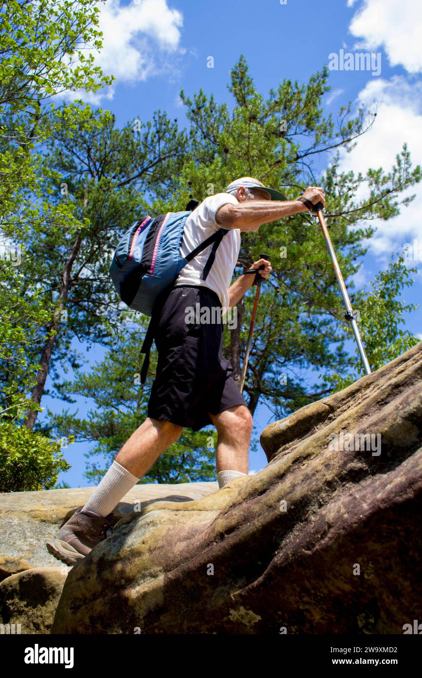 Une vue à angle bas d'un homme âgé marchant dans les bois, portant un sac à dos, avec un ciel bleu nuageux en arrière-plan, à Red River gorge KY Banque D'Images