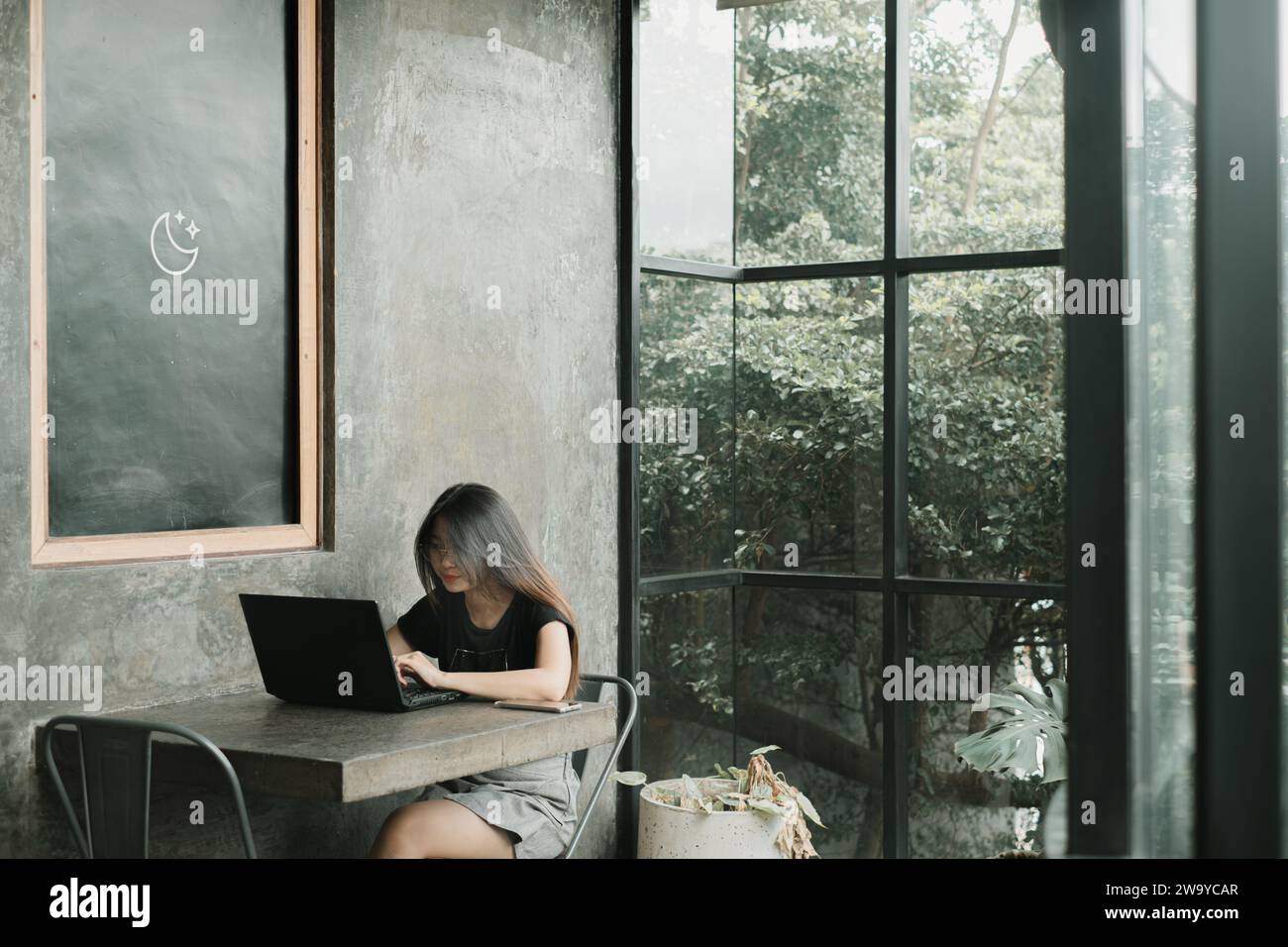 Jeune femme asiatique utilisant une tenue décontractée travaille sur un ordinateur portable dans une salle industrielle ou un café Banque D'Images