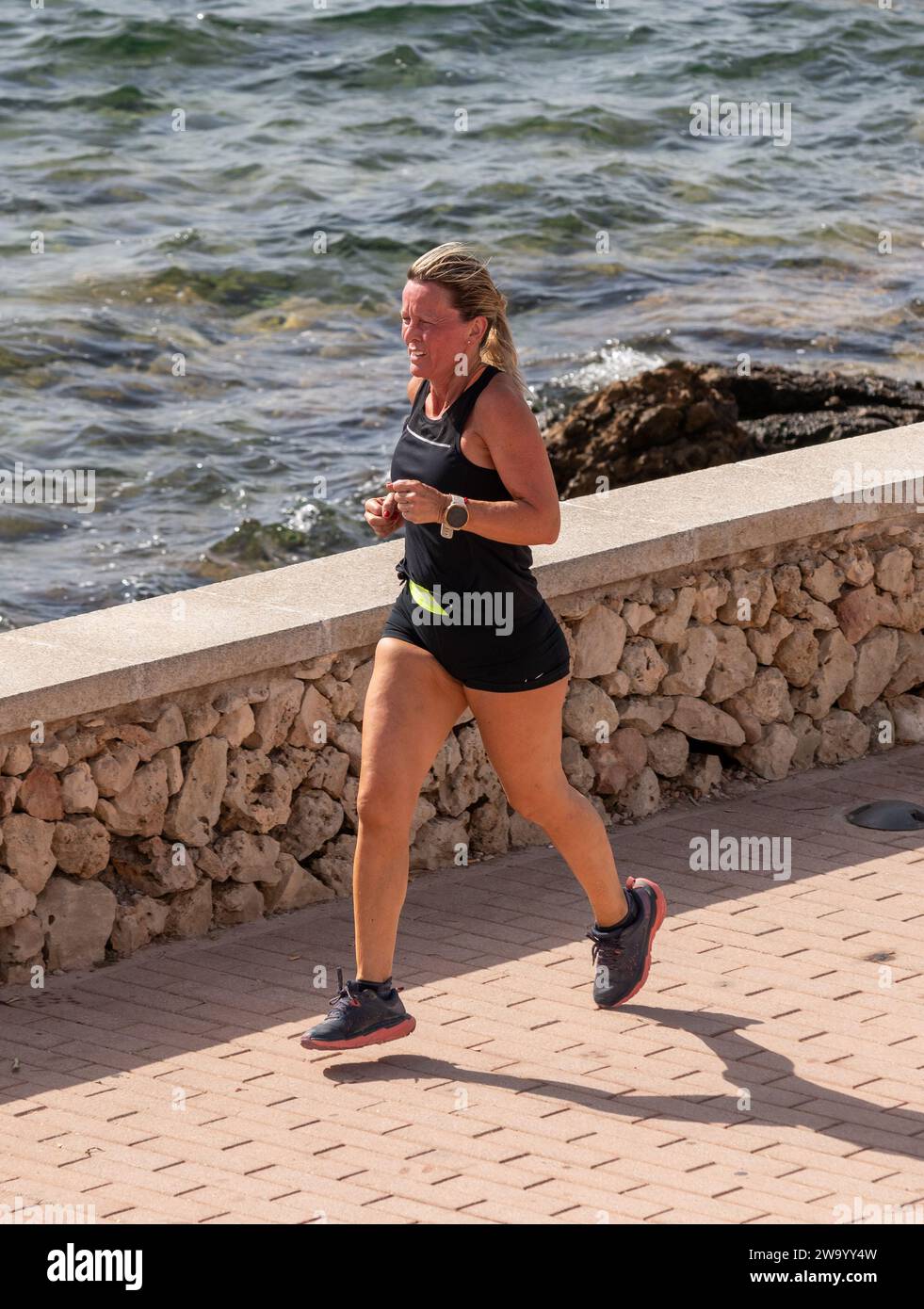 Un jogger féminin sur le front de mer Fornells Menorca Espagne Banque D'Images