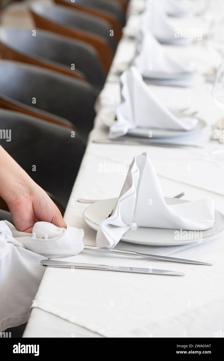 Membre du personnel polissant méticuleusement l'argenterie en préparation d'un dîner formel, technique visant à affiner l'expérience culinaire des invités Banque D'Images