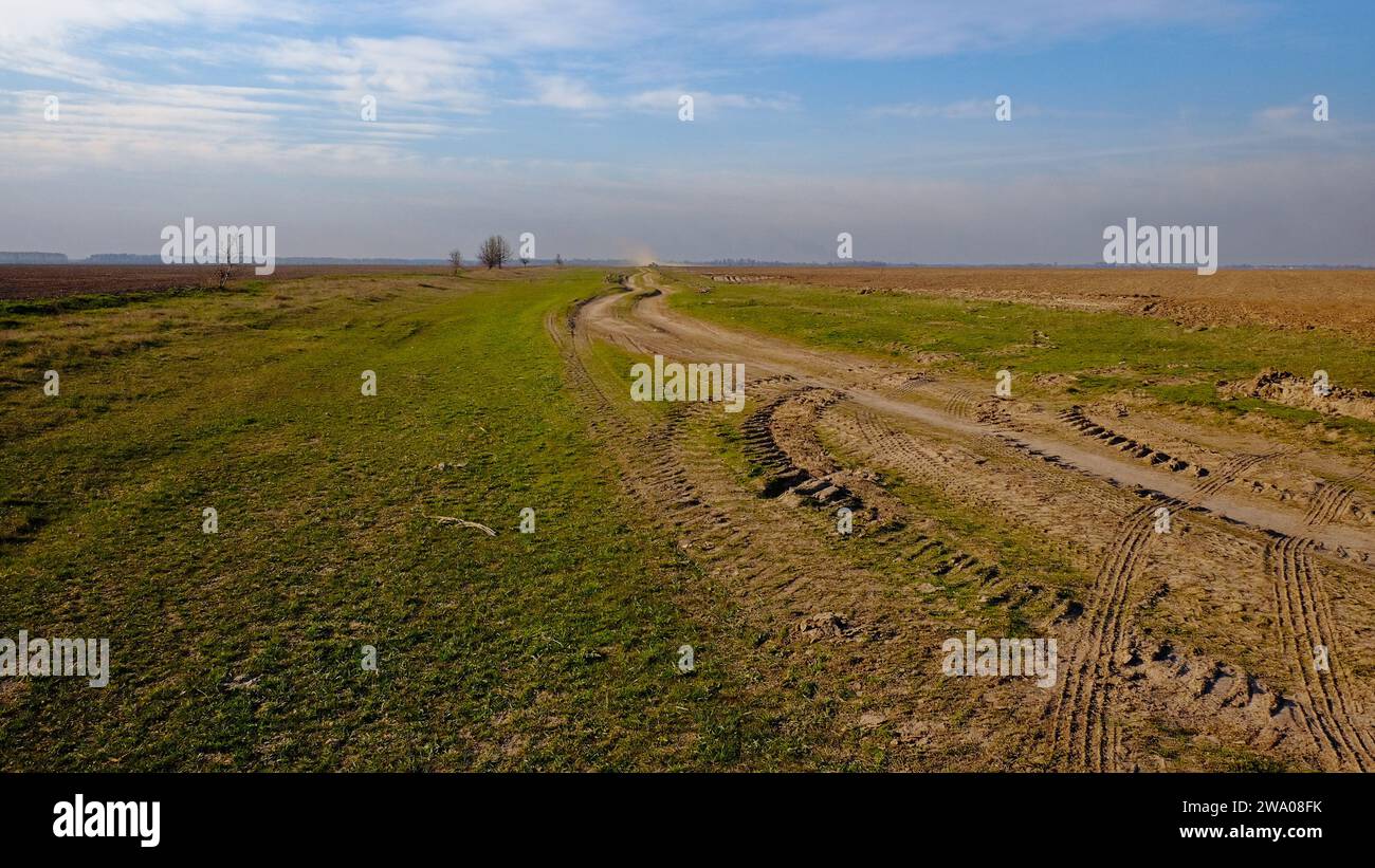 Un vaste espace ouvert avec de la verdure et un chemin de terre marqué par des pistes de véhicules. Banque D'Images