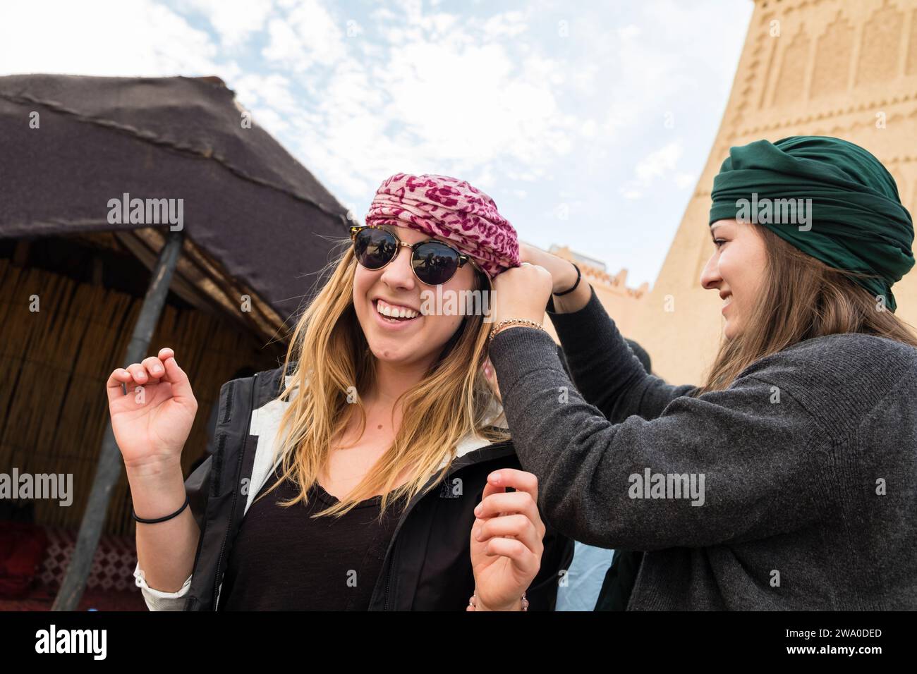 Une touriste aide une autre femme à attacher une écharpe dure du désert sur sa tête pour la protéger dans le désert du Sahara, au Maroc Banque D'Images