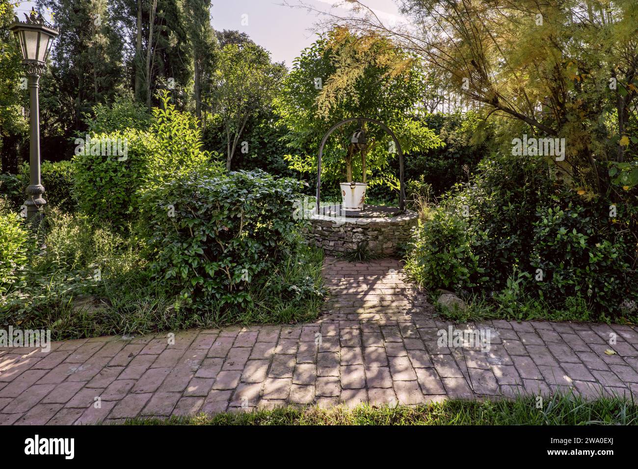 Un puits avec un seau en métal étamé blanc dans un jardin avec un chemin carrelé Banque D'Images