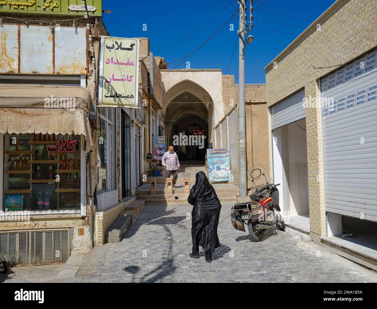 Femme musulmane vêtue de tchador noir traditionnel marche dans une entrée étroite du Grand Bazar de Kashan, Iran. Banque D'Images