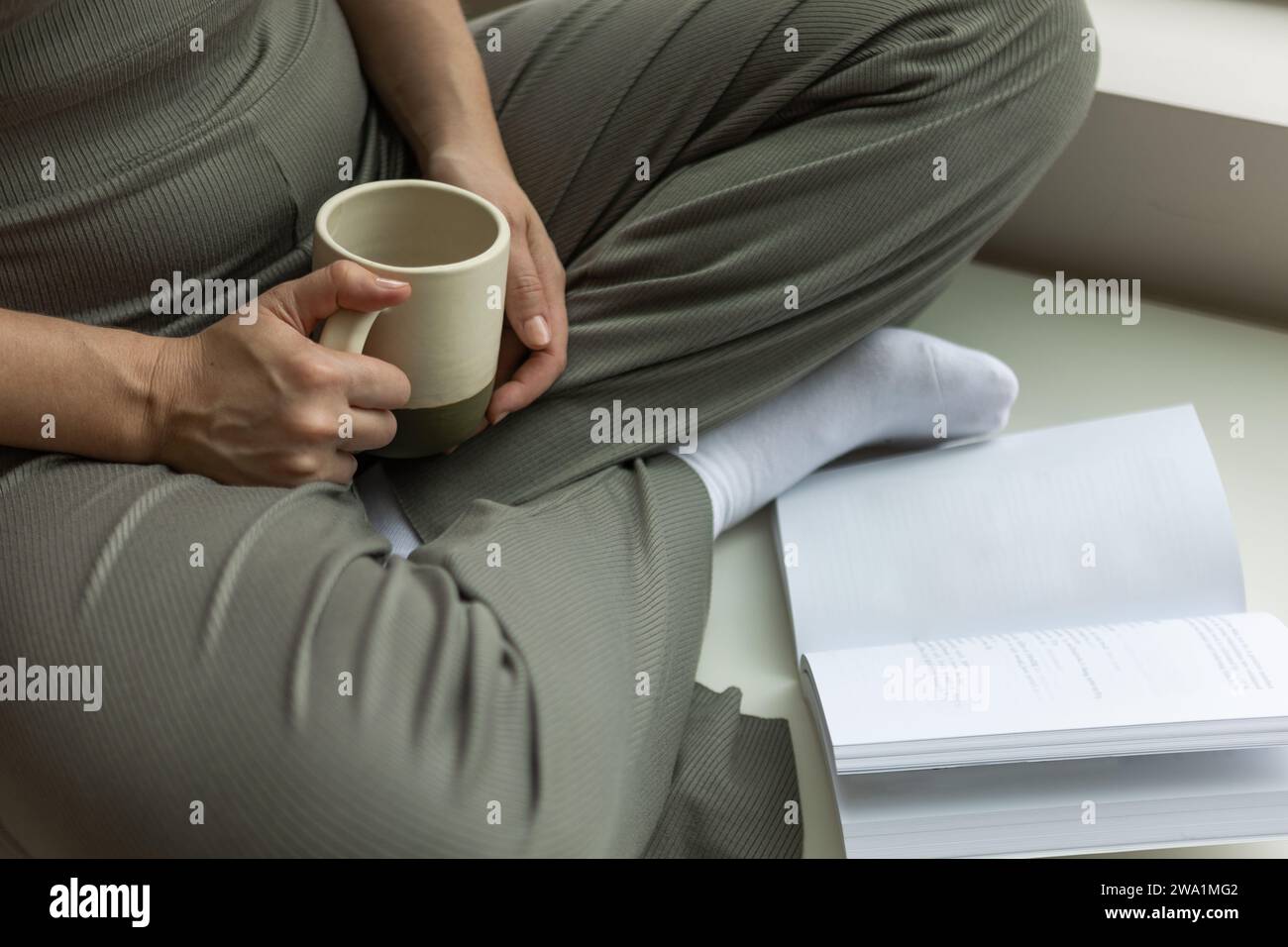 Femme assise les jambes croisées appréciant le café du matin tout en lisant un livre Banque D'Images