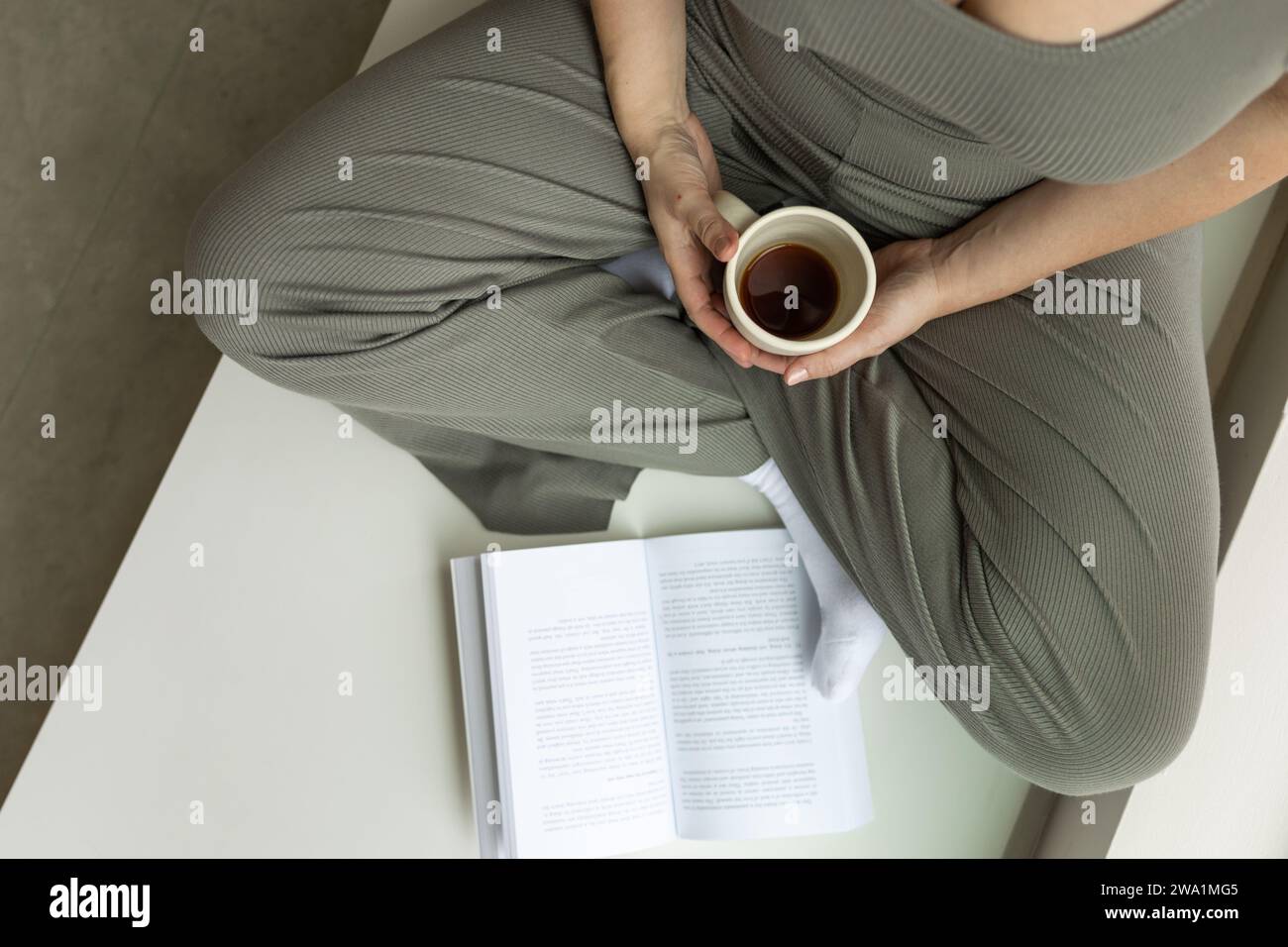 Femme à jambes croisées apprécie le café du matin tout en lisant un livre Banque D'Images