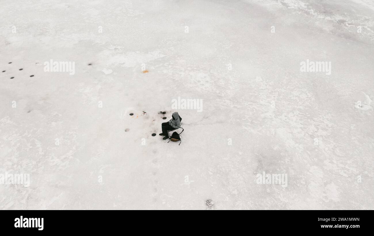 Garçon célibataire assis près du trou de pêche sur glace attendant une bouchée sur le lac gelé Banque D'Images