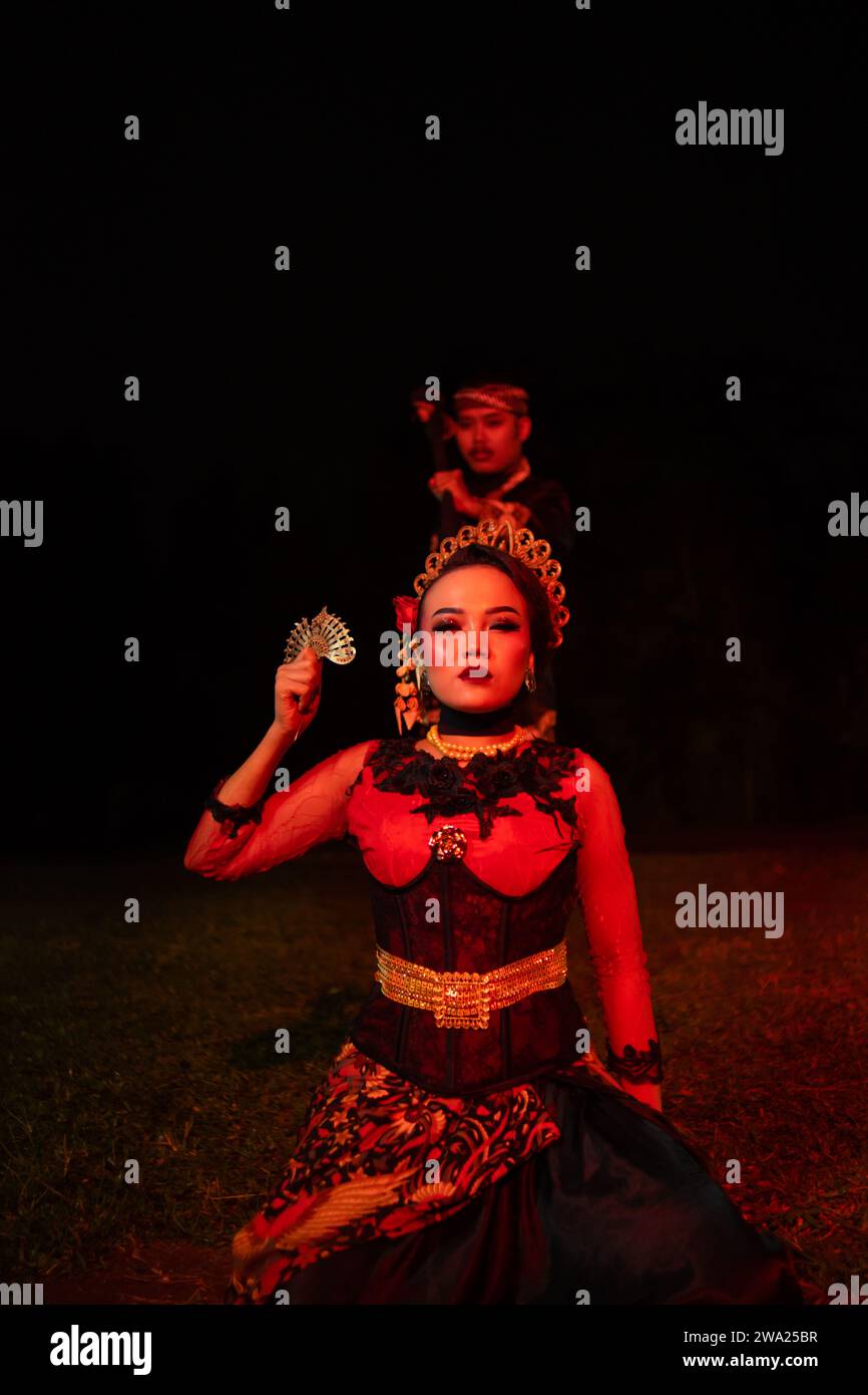 une danseuse en costume rouge s'assit dans le silence de la nuit qui renforça la tristesse au milieu du champ Banque D'Images