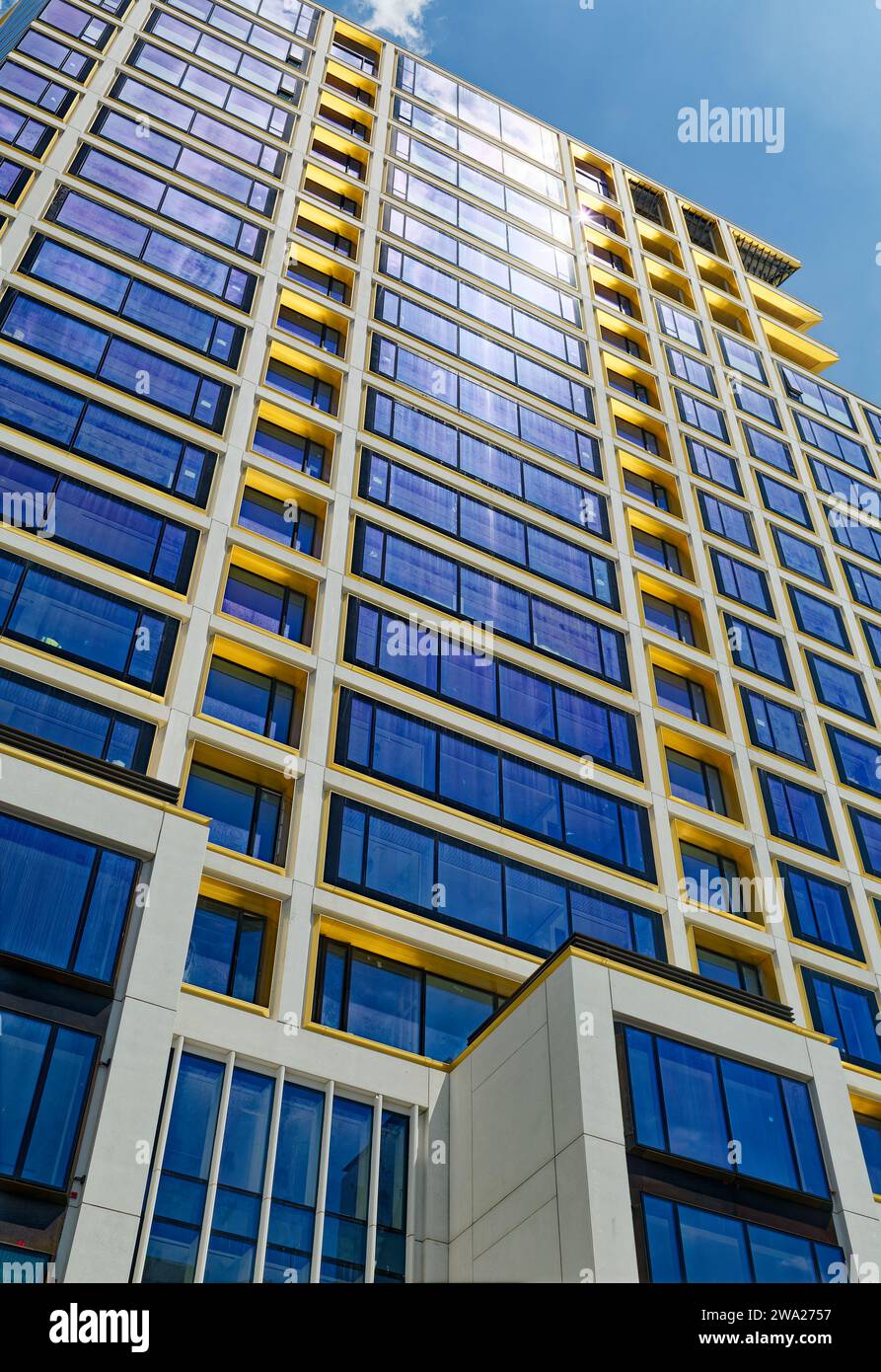 Le ciel bleu réfléchi, les garnitures en bronze jaune et le béton blanc foncé créent des motifs saisissants au 551 West 21st Street, un condominium résidentiel. Banque D'Images