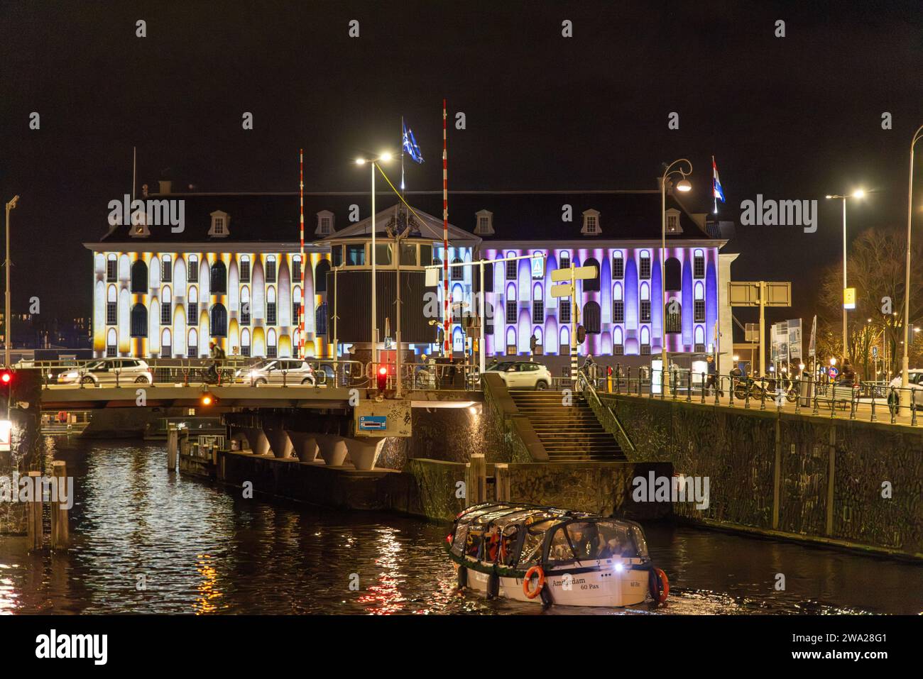 Vue nocturne sur le Musée maritime (Scheepvaartmuseum) Amsterdam, avec projection de lumière sur la façade pendant le Festival des lumières d'Amsterdam ; bateau d'excursion au premier plan : Banque D'Images