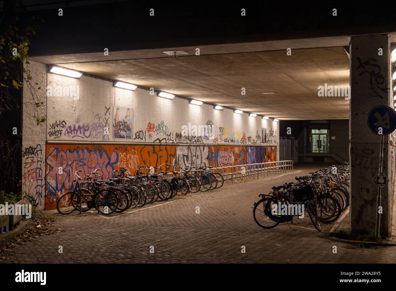 Vue nocturne du tunnel éclairé (passage souterrain) avec vélos stationnés et graffitis sur les murs Banque D'Images