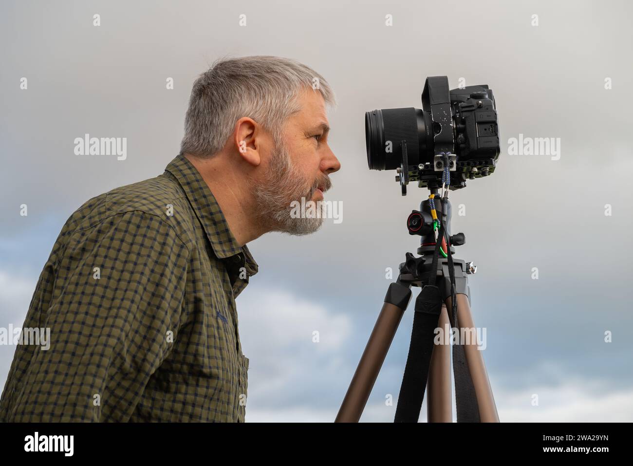 Photographe, cheveux gris et barbe pleine, 56 ans, regardant dans son appareil reflex 35mm sur le trépied, ciel couvert gris Banque D'Images