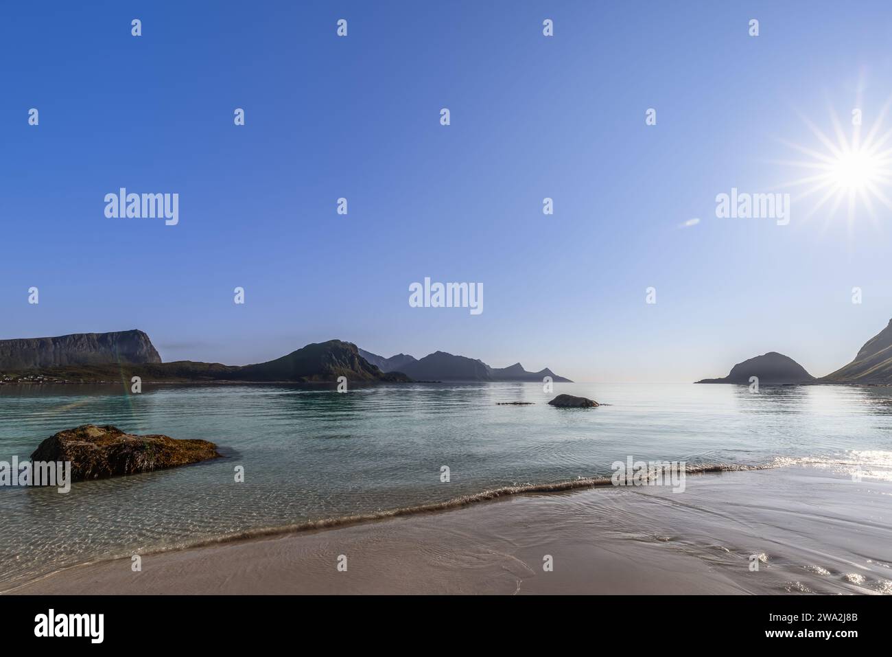 Soleil scintillant le matin sur la paisible plage de Haukland en Norvège, avec des eaux claires et des îlots rocheux sur fond de montagne. Île Lofoten Banque D'Images